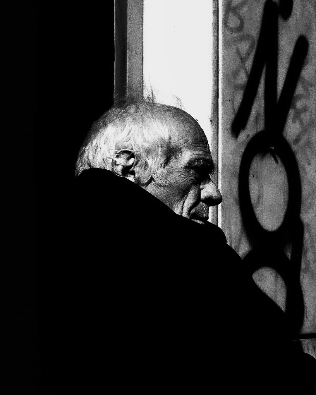 An old man in profile beside a graffitied wall