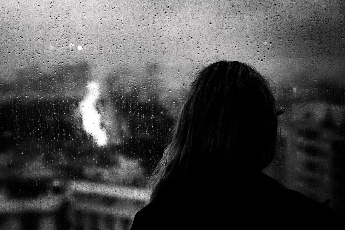 A woman behind a rain-streaked window